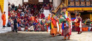 Público en el patio exterior del dzong de Paro, con danzantes del Tsechu y su colorido traje tradicional de seda, sombreros negros y calaveras y tambores, en Bután (Bhutan)