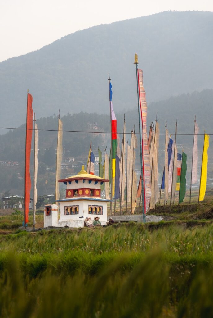 Banderas de oración en el valle de Punakha, Bután (Bhutan) junto a un pequeńo chorten o estupa donde descansan unos agricultores butaneses