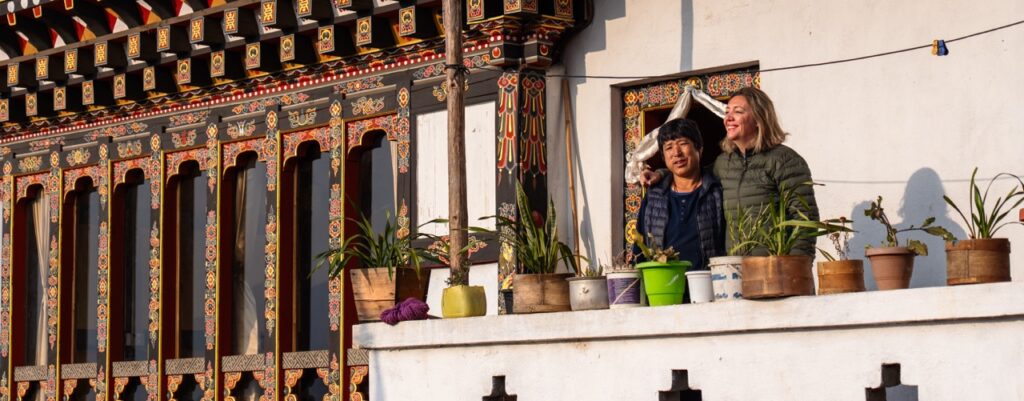 Turista y local butanesa en la entrada de una farmhouse tradicional de Bután (Bhutan) en el valle de Phobjikha