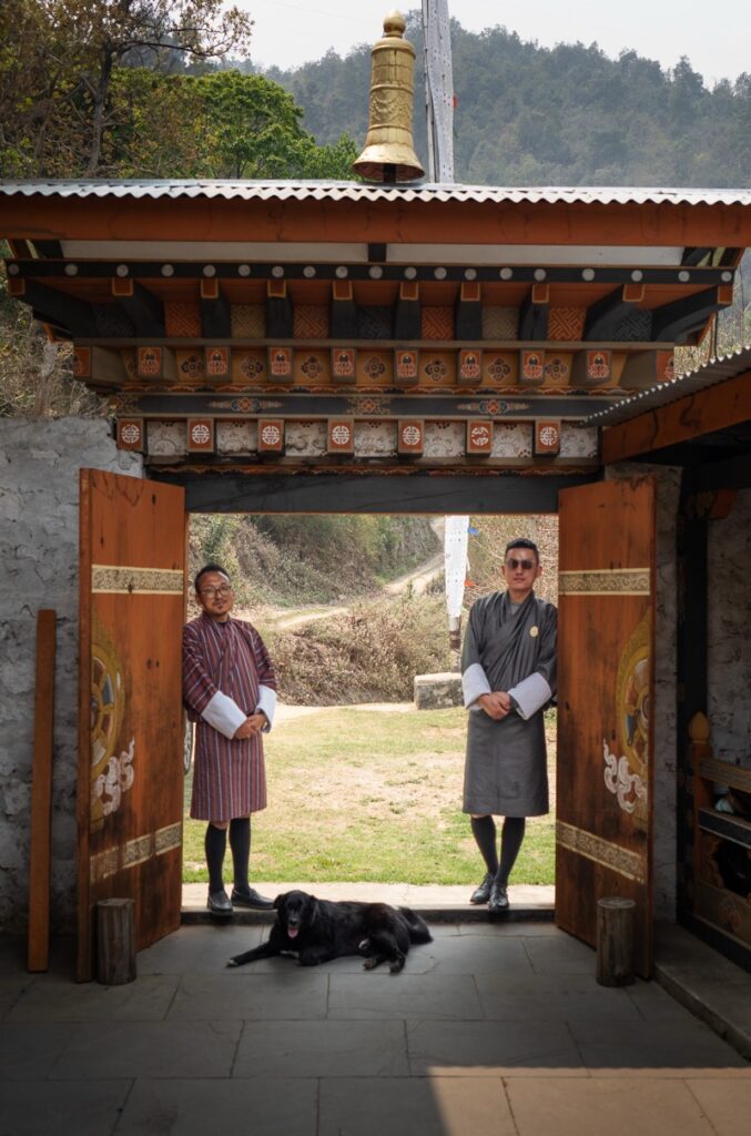Guias turisticos de Bután (Bhutan) apoyados en una puerta decorada típica butanesa y llevando sus tradicionales trajes "gho"