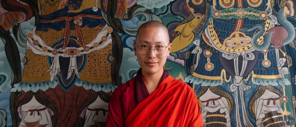 Monja budista apoyada en un colorido mural del convento Sangchhen Dorji Lhuendrup Nunnery en Punakha