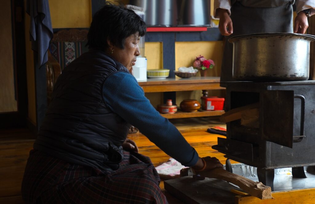 Mujer butanesa enciende el fogón de leña en su casa rural o farmhouses de Bután (Bhutan)
