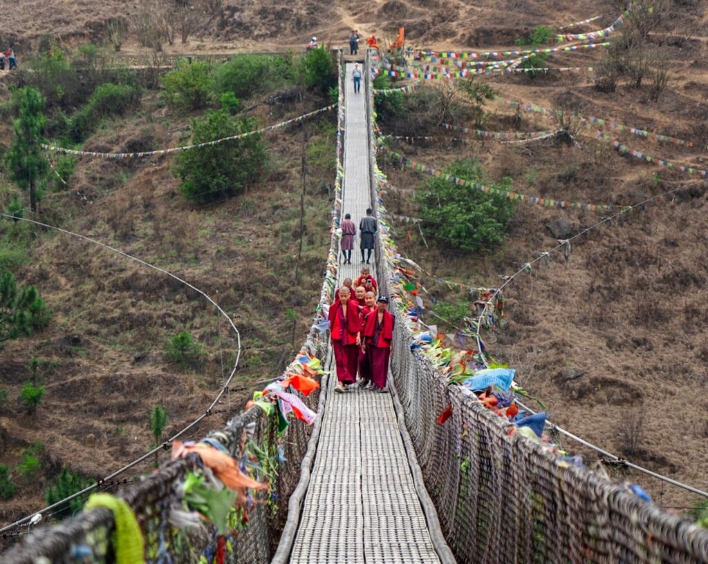 Monjes cruzando el puente colgante de Punakha en Bután (Bhutan), rodeados de banderas de oración